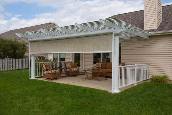A pristine and well-kempt backyard patio, sheltered above by a pergola and on the sides via a retractable screen.