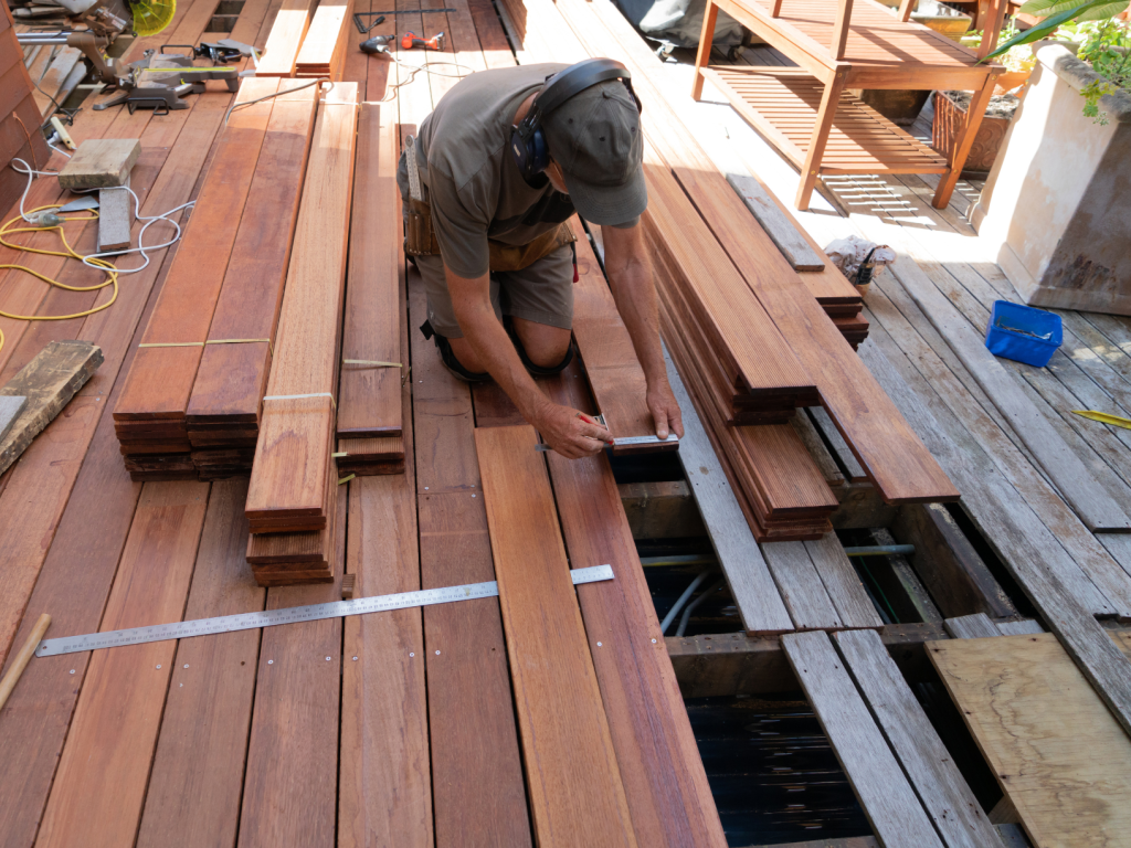 A deck builder hard at work on a deck restoration project, replacing old planks of wood.