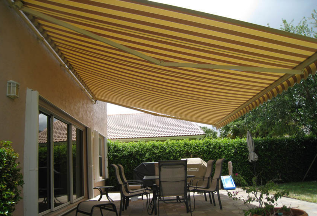 A red and mustard striped awning by Sunesta, providing ample shade for a homeowner's backyard patio.