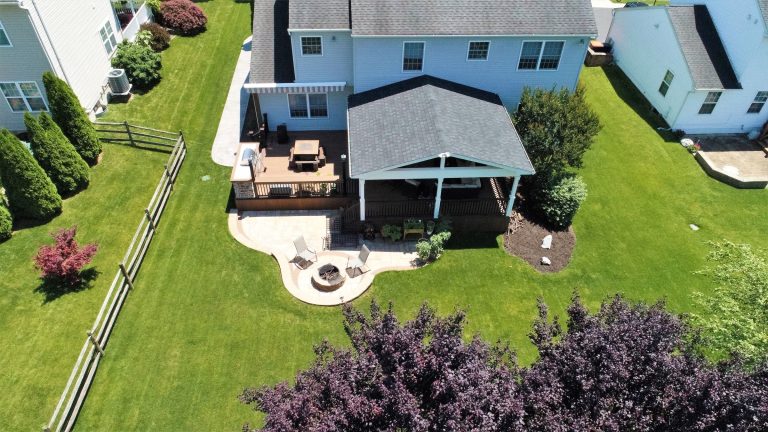 Aerial view of a backyard with a roof structure, deck and curved paver patio