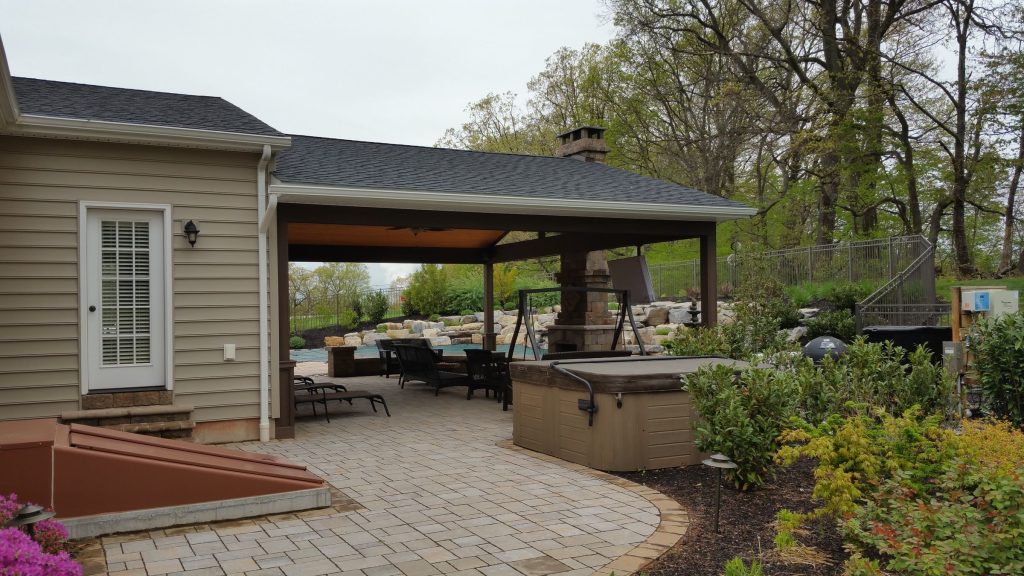 Paver patio leading to an open pavilion with a stone fireplace